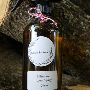 Pode incluir: Uma garrafa de vidro marrom com um bico de pulveriza&ccedil;&atilde;o preto e um r&oacute;tulo branco que diz "Simply By Anne" e "Pillow and Room Spray Citrus".