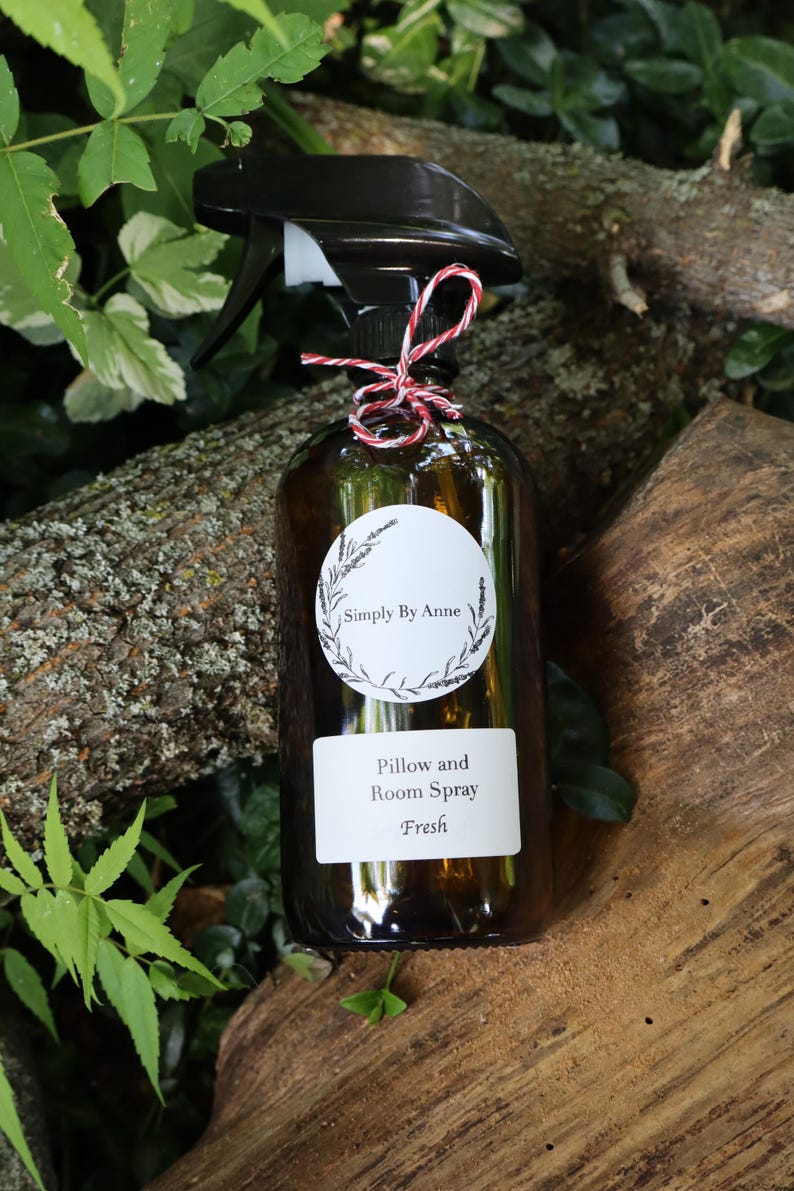 Pode incluir: Uma garrafa de vidro marrom com um bico de pulveriza&ccedil;&atilde;o preto e um r&oacute;tulo branco que diz "Simply By Anne" e "Pillow and Room Spray Fresh". A garrafa est&aacute; amarrada com um cord&atilde;o vermelho e branco.