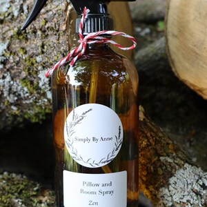 Pode incluir: Uma garrafa de vidro marrom com um bico de pulveriza&ccedil;&atilde;o preto e um r&oacute;tulo branco que diz "Simply By Anne Pillow and Room Spray Zen". A garrafa est&aacute; amarrada com um barbante vermelho e branco.