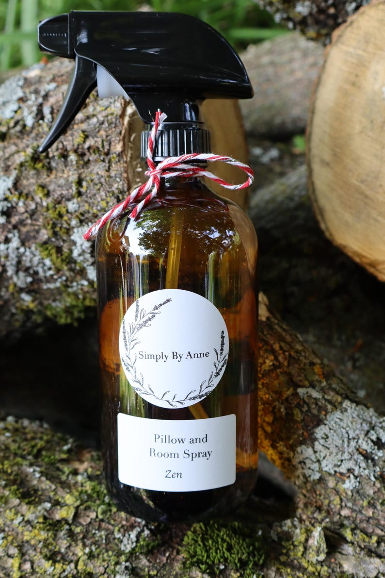 Pode incluir: Uma garrafa de vidro marrom com um bico de pulveriza&ccedil;&atilde;o preto e um r&oacute;tulo branco que diz "Simply By Anne Pillow and Room Spray Zen". A garrafa est&aacute; amarrada com um barbante vermelho e branco.