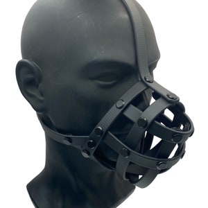 May include: Black leather muzzle with a cage design and metal rivets. The muzzle is worn on a mannequin head.