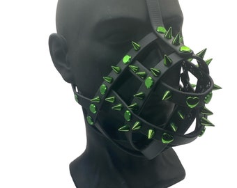 May include: A black leather muzzle with green metal spikes and studs. The muzzle has a heart-shaped design on the front.