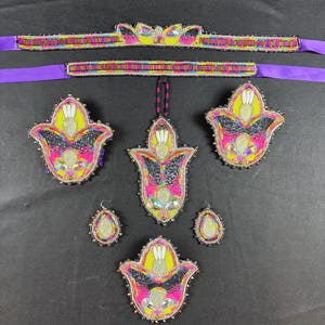 May include: A set of beaded accessories featuring a purple ribbon headband, a central pendant, and four floral-shaped ornaments in neon yellow, hot pink, black, and iridescent accents. The pieces are decorated with intricate seed bead embroidery.