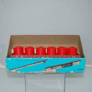 May include: A vintage model train set featuring six red tank cars and a brown box. The box has a blue and white design with text. The set is likely a collectible item for train enthusiasts.