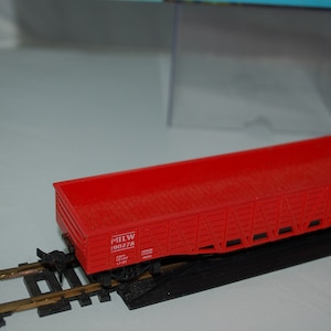 May include: A red model train boxcar with the text "MILW 190228" on the side. The boxcar is on a black track and sits on a section of model train tracks.