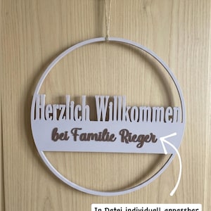 Puede incluir: Un letrero de bienvenida circular blanco con el texto alemán "Herzlich Willkommen bei Familie Rieger" y el texto "In Datei individuell anpassbar". El letrero está colgado en una puerta de madera.