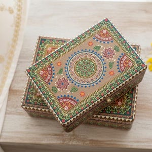 May include: Two rectangular wooden boxes with detailed hand-painted designs. The lids display a central mandala with floral and geometric patterns in green, red, blue, and orange on a tan base. The edges are decorated with intricate borders.