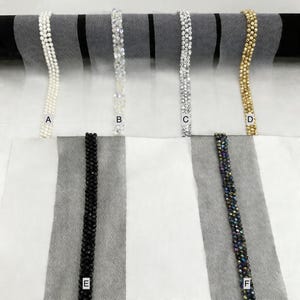 May include: A selection of beaded trims in various styles. The trims include white pearls, clear crystals, silver crystals, gold beads, black beads, and iridescent beads. The trims are displayed against a white and black striped background.