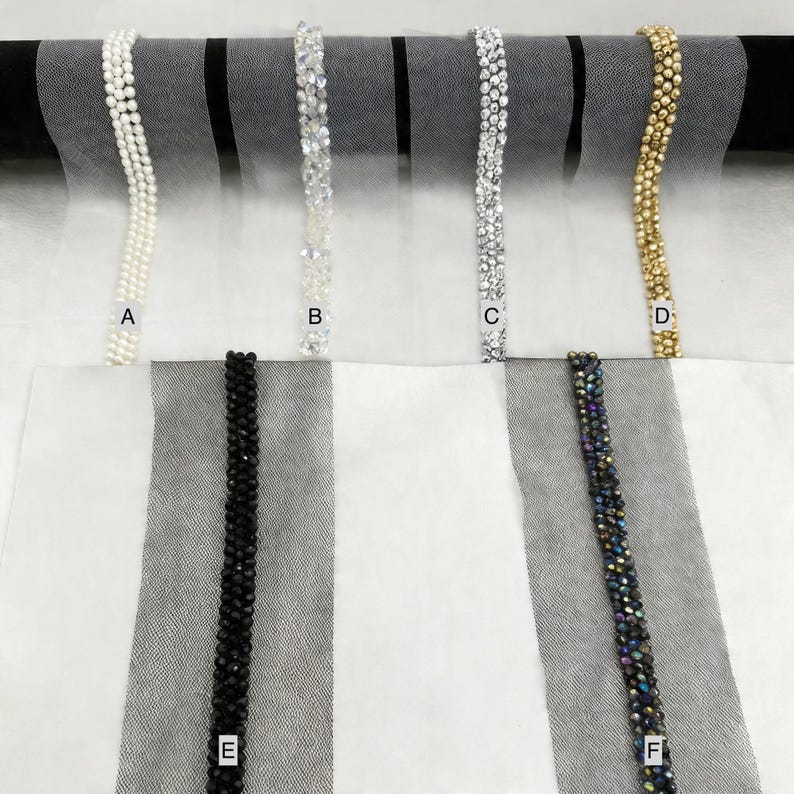 May include: A selection of beaded trims in various styles. The trims include white pearls, clear crystals, silver crystals, gold beads, black beads, and iridescent beads. The trims are displayed against a white and black striped background.