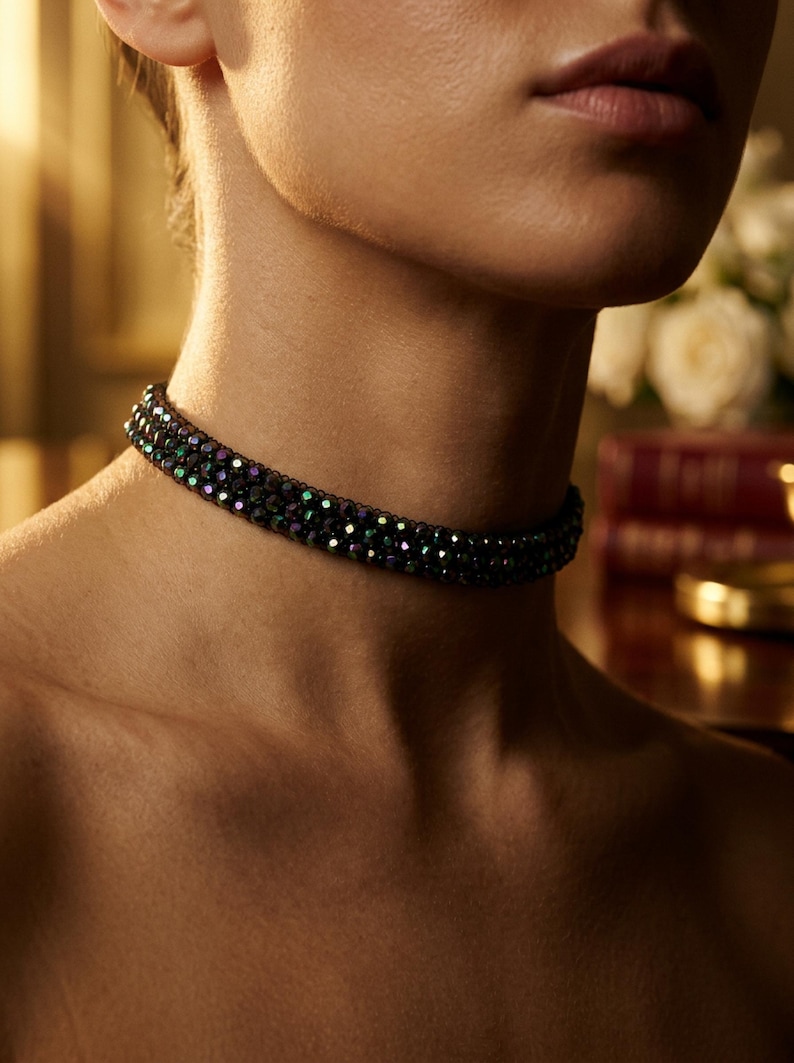 May include: A close-up of a black beaded choker necklace with iridescent green and purple accents. The necklace is worn around the neck. The background is blurred, with soft lighting.