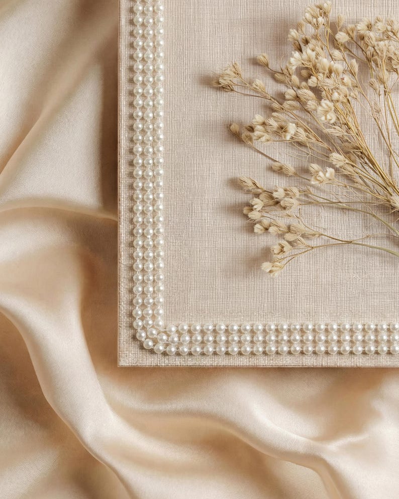 May include: A rectangular, beige-colored box with a pearl border. Dried, light-brown flowers rest on the box. The background is a cream-colored, silky fabric, creating a soft, elegant aesthetic.