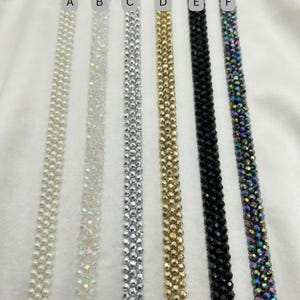 May include: A selection of six beaded trim ribbons in various colors. The ribbons include white pearl, iridescent, silver, gold, black, and iridescent multi-color. The ribbons are displayed on a white background.