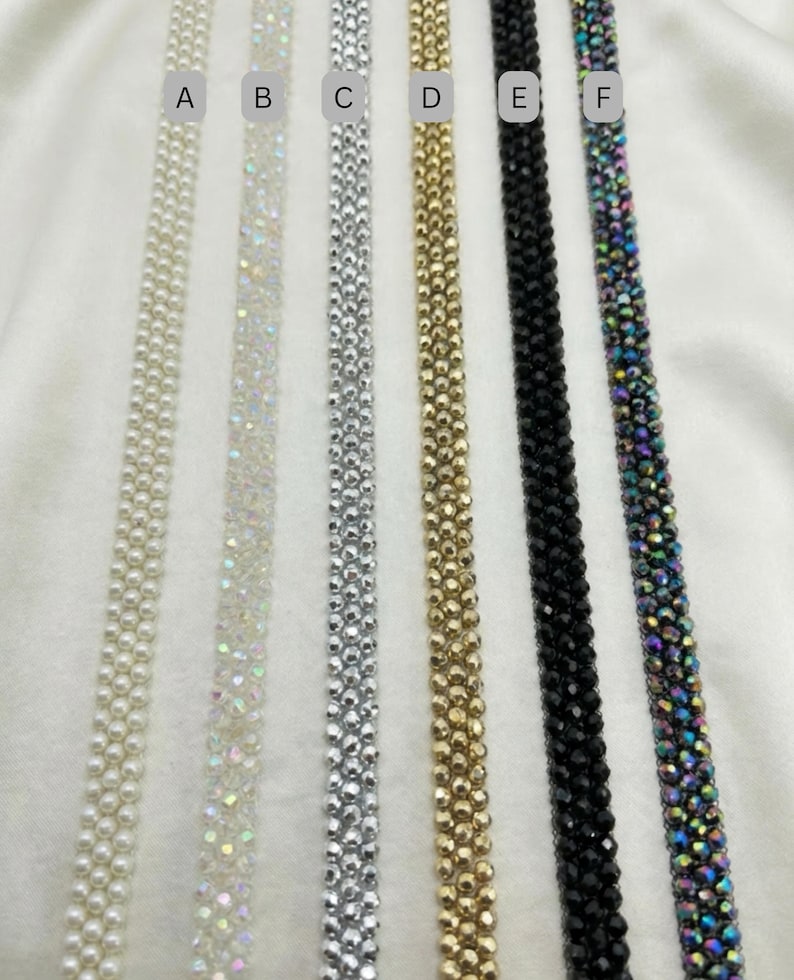 May include: A selection of six beaded trim ribbons in various colors. The ribbons include white pearl, iridescent, silver, gold, black, and iridescent multi-color. The ribbons are displayed on a white background.