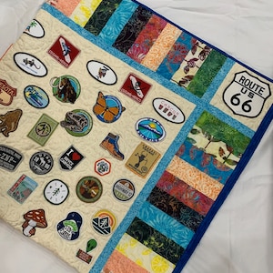 以下が含まれることがあります： ベージュのキルトに、さまざまな色のパッチが縫い付けられています。パッチには、蝶や動物の画像、テキストが描かれています。キルトは青い縁取りで飾られています。パッチのテキストには、「Route US 66」、「Utah 1896」、「Bryce Canyon」、「Cozumel Mexico」、「Anasazi」、「Cancun」、「Minnesota」、「Zion National Park」、「Highway 12」、「Shroom Queens」などが含まれています。
