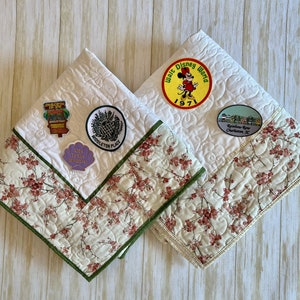 May include: Two white quilted fabric squares with green trim. One square features a Mickey Mouse patch with the text "Walt Disney World 1971" and a patch with the text "Rainbow Row Charleston, SC". The other square features a patch with the text "Middleton Place" and a patch with the text "Life is the Bubble".