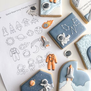 Puede incluir: Un conjunto de galletas de azúcar con temática espacial decoradas con glaseado azul, blanco y naranja. Las galletas representan astronautas, cohetes, planetas y estrellas. Una galleta tiene la palabra "ONE" escrita en ella. Otra galleta tiene el texto "Harrison's first trip around the sun".