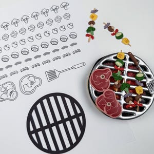 May include: A miniature silver-colored circular grill with red and brown food items, including steaks and vegetable skewers. Beside it are two small skewers, a black circular grill cutout, and a white sheet with black line drawings of food.