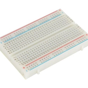 May include: A white breadboard with numerous small holes for electronic components. The board has red and blue lines along the top and bottom, with plus and minus symbols. Letters and numbers are printed on the board.