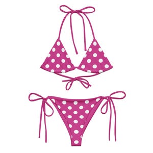 May include: A two-piece swimsuit in a vibrant fuchsia color, adorned with a white polka dot pattern. The top is a halter style, and the bottom is a classic bikini cut. The swimsuit is tied with matching fuchsia strings.