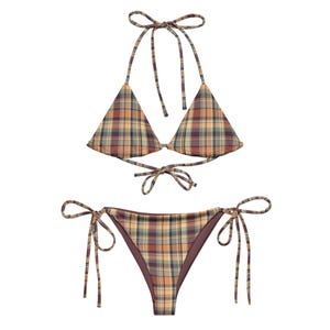 May include: A two-piece bikini set with a plaid pattern in shades of orange, brown, and green. The top is a halter style with triangle cups and tie closures. The bottoms are a classic tie-side style.