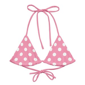 May include: Pink bikini top with white polka dots. The top features triangle cups with tie closures at the neck and back. The swimwear is designed with a playful, feminine aesthetic.