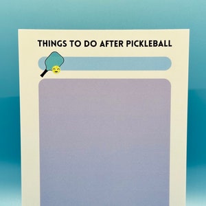 Op de afbeelding: Een witte afdrukbare checklist met de tekst "Things to do after pickleball" en een afbeelding van een blauw en geel pickleball-bat. Er staan drie gele smiley-gezichten onderaan de checklist.