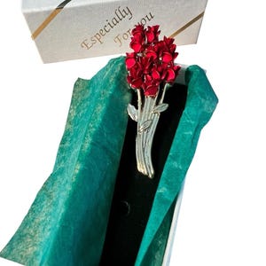 May include: A silver-toned metal brooch shaped like a bouquet of red flowers with green leaves, resting inside a white rectangular gift box lined with green tissue paper. The box lid features the text Especially For you in gold script lettering.