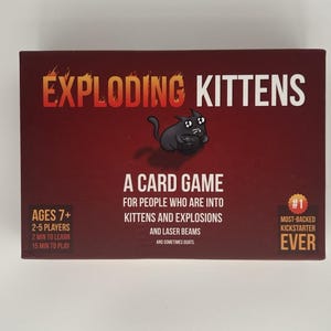 Op de afbeelding: Een witte keramische mok met een zwarte handgreep en de tekst "But First, Coffee" in een vetgedrukte, zwarte letter. De mok staat tegen een wazige achtergrond, wat een gezellige setting suggereert.