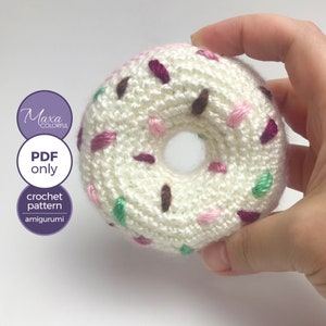 Op de afbeelding: Een gehaakt donut amigurumi patroon. De donut is wit met roze, groene en bruine sprinkels. Het patroon is beschikbaar als PDF-download.