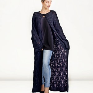 May include: A long, navy blue knitted cardigan with a cable knit pattern and openwork design. The cardigan is open in the front and has a loose fit.