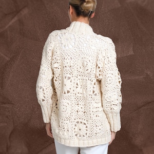 May include: A white crocheted cardigan with a square pattern. The cardigan has long sleeves and a loose fit.