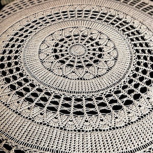 May include: A white crocheted doily with a circular design. The doily has a delicate, intricate pattern with a central circle and radiating spokes.