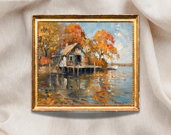 May include: Oil painting of a lakeside cabin in autumn. The cabin, with a weathered appearance, is set on stilts over the water. The scene is framed by trees with vibrant orange and yellow foliage, reflecting in the water. The painting is in a gold frame.