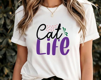 May include: White t-shirt with the words "Cat Life" in a playful design. The word "Cat" is in black script with red star accents, and "Life" is in purple block letters. Green leaf accents complete the design.