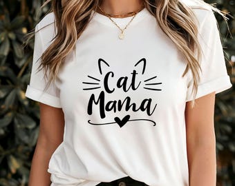 May include: White t-shirt with the text "Cat Mama" in a black, stylized font. The design includes cat ears and whiskers above the text, and a heart below. The shirt has short sleeves.