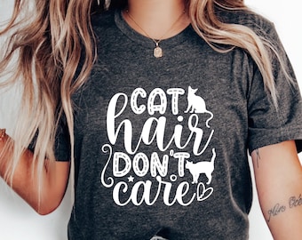 May include: A gray t-shirt with the text "Cat hair don't care" in white lettering. The text is surrounded by a white outline and includes two white silhouettes of cats.