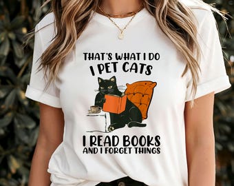 May include: White t-shirt with a black cat reading a book and the text "That's what I do I pet cats I read books and I forget things."