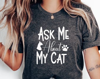 May include: A dark gray t-shirt with white text that reads "Ask Me About My Cat" with a cat silhouette and paw print graphic.