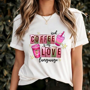 May include: White t-shirt featuring a pink and green graphic design that reads "iced coffee is my love language". The design includes two cups of coffee and a pink and green swirl.