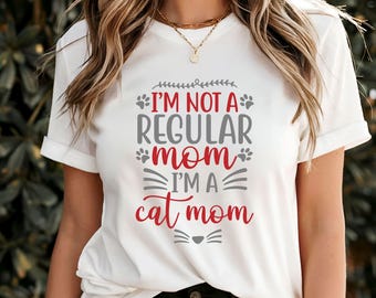 May include: White t-shirt with a gray and red graphic that says "I'm not a regular mom I'm a cat mom" with paw prints and a cat face.