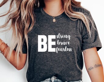 Op de afbeelding: Een grijs T-shirt met de tekst "BE strong brave fearless" in wit.