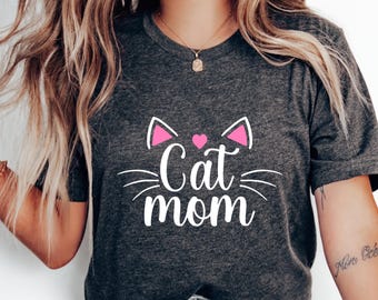 May include: A gray t-shirt with a white graphic of a cat face with pink ears and a pink heart. The text "Cat mom" is written below the cat face.