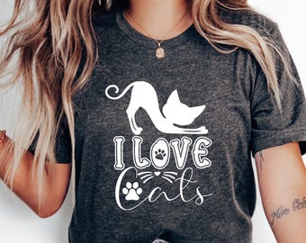 Peut inclure: T-shirt gris foncé avec l'inscription blanche "I Love Cats". Le motif comprend une silhouette de chat blanc et des empreintes de pattes. Le t-shirt est fait d'une matière douce.