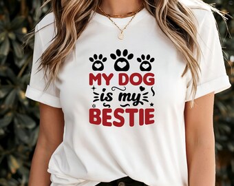 Op de afbeelding: Wit T-shirt met een zwarte en rode afbeelding met de tekst "My dog is my bestie" met poot afdrukken en harten.