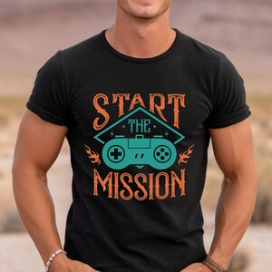 May include: Black t-shirt with a graphic design of a video game controller and the text "Start the Mission" in orange.