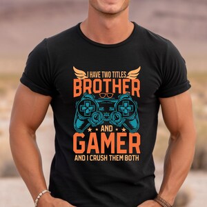 May include: Black t-shirt with a graphic design of a video game controller and the text "I have two titles: Brother and Gamer and I crush them both."