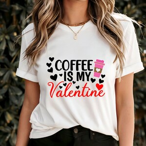 Op de afbeelding: Wit T-shirt met zwarte tekst die "Coffee is my Valentine" luidt en een roze koffiebekergrafiek met harten.