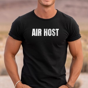 以下が含まれることがあります： 前面に白い文字で「AIR HOST」とプリントされた黒いTシャツです。
