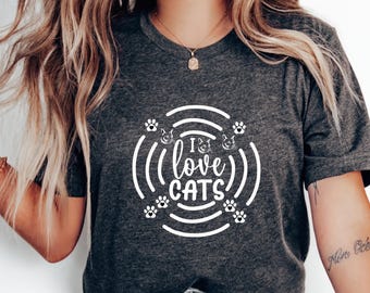 Peut inclure: Un t-shirt gris foncé avec un motif graphique blanc qui dit "I (love) cats" dans un cercle avec des empreintes de pattes autour.