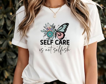 May include: White t-shirt featuring a butterfly and floral design. The text "SELF CARE is not selfish" is printed on the shirt.